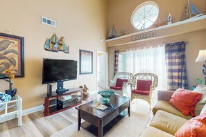 Una sala de estar con televisión, sillas de mimbre, un sofá y una ventana con cortinas.