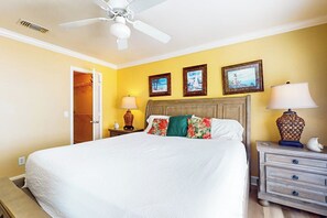 A hotel room with a bed, a nightstand, a lamp, a ceiling fan, and a door leading to a bathroom. - Dawn Condominiums - Break of Dawn (Galveston)