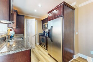A kitchen with dark wood cabinets, stainless steel appliances, and a granite countertop. - Dawn Condominiums - Break of Dawn (Galveston)