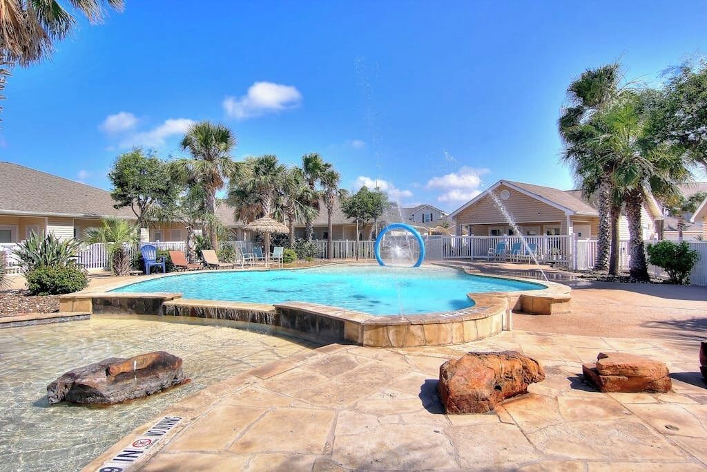 A swimming pool with a water slide, surrounded by palm trees and lounge chairs.