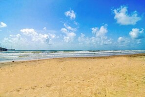Uma praia com céu claro e um píer ao longe.