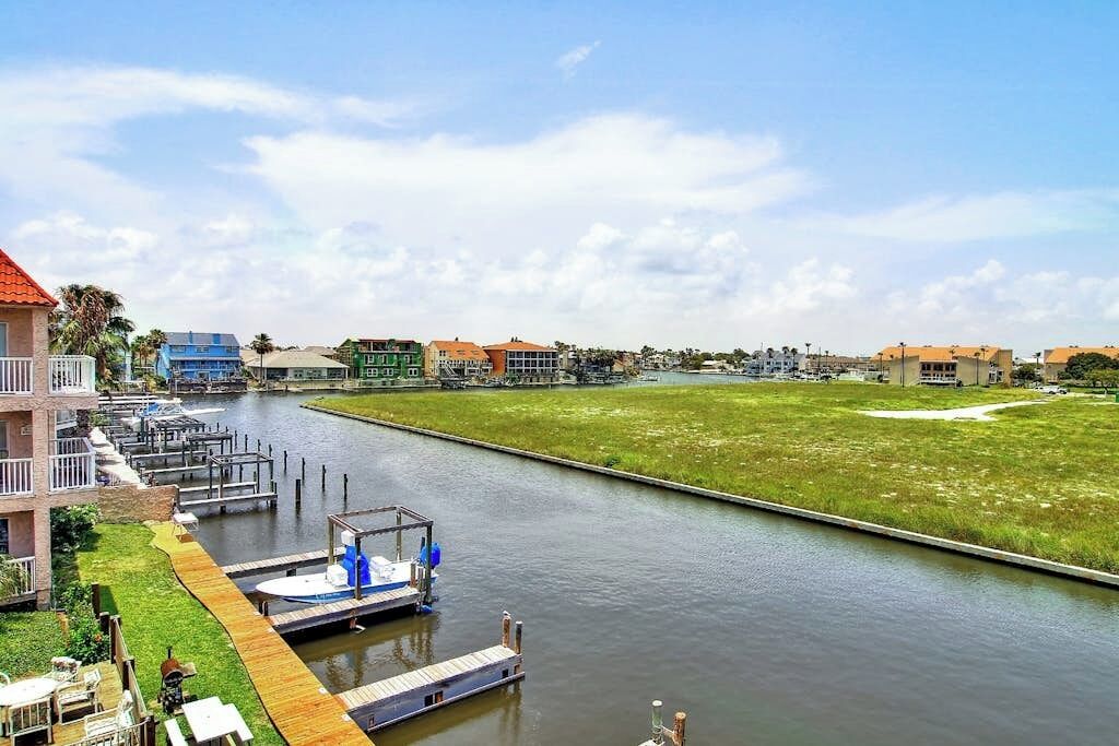 A marina with docked boats, a grassy area, and buildings in the background.