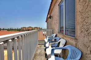 Ein Balkon mit Geländer, einem Fenster und mehreren Plastikstühlen.