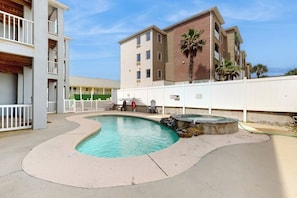 A swimming pool with a curved edge, a small waterfall feature, and a white fence surrounding the area. - Padre Island 104 - Ocean Views, Walk to the Beach (Corpus Christi)