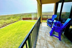 A balcony with a view of the ocean, a grassy lawn, and blue chairs. - The Beach Condo #204 (South Padre Island)