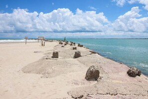 Ein Strand mit einem Felssteg, einer Holzbank und einem Schild.