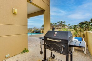 En grill med ett sidobord, en pool i bakgrunden och utsikt över palmer och byggnader.