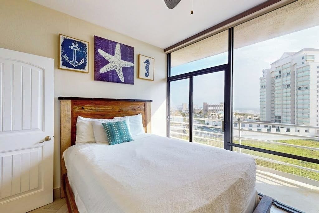Ein Hotelzimmer mit einem großen Bett, einem Holzkopfstück und Blick auf eine Stadtlandschaft durch ein großes Fenster.