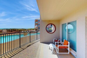 A balcony with a pool view, a round mirror, and two chairs. - Suntide II Condominiums #108 (South Padre Island)