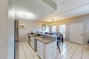 A kitchen with a central island, a refrigerator, and a dining area with chairs. - Coronado Condominiums #201 (South Padre Island)