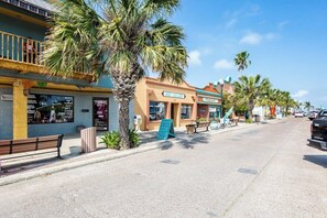 Eine Straße mit Palmen, einer Bank und Geschäften, darunter eine Kunstgalerie und ein Café.