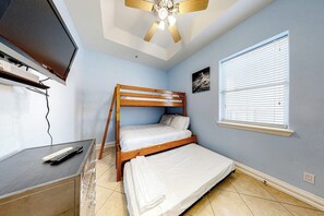 A room with a bunk bed, a desk with a keyboard, a television, and a ceiling fan. - Island Serenity - Pool, Steps to Beach, Dogs OK (South Padre Island)