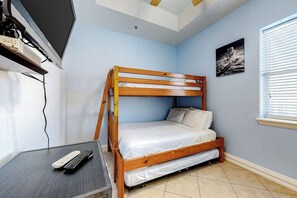 Ein Zimmer mit einem Etagenbett, einem Schreibtisch mit Computer und Fernbedienung, einem Fernseher und einem Bild an der Wand.