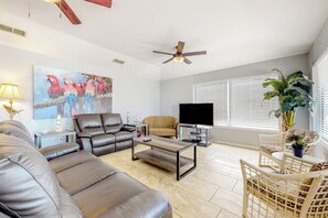 Ein Wohnzimmer mit Ledersofas, einem Couchtisch, einem Fernseher und einem Deckenventilator.