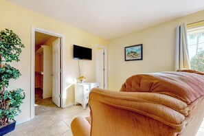 Ein Zimmer mit einem Bett, einem Fernseher, einem Gemälde und einer Zimmerpflanze.
