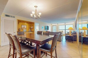 Un vaste espace dédié à la salle à manger, avec une grande table et des chaises en bois, un lustre, et une vue sur le salon, qui comprend un canapé et des lampes.