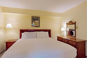 Ein Hotelzimmer mit einem großen Bett, einem Nachttisch, einer Nachttischlampe, einem wandmontierten Spiegel und einem gerahmten Bild an der Wand.