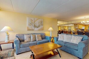 Ein Wohnzimmer mit zwei Sofas, einem Couchtisch und Lampen. Es gibt einen Essbereich mit Stühlen und einer Chandelier.