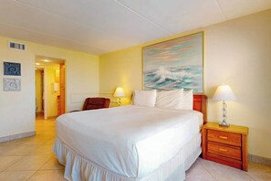 A hotel room with a large bed, two bedside lamps, a painting of a seascape, and a chair. - Saida Towers IV #4906 (South Padre Island)