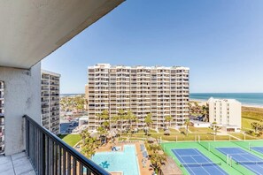 Un hôtel de grande hauteur doté de nombreux balcons, d’une piscine, de courts de tennis et offrant une vue sur la plage.