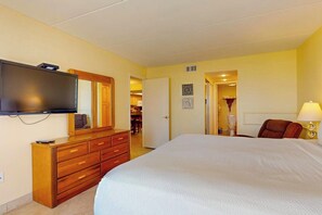 Une chambre d’hôtel avec un grand lit, un téléviseur fixé au mur, une commode en bois et une porte donnant accès à une salle de bain.