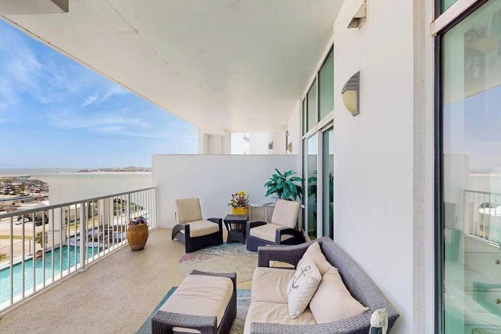 A balcony with outdoor seating, a view of the sea, and a glass railing.