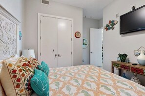 A bedroom with a bed, a wardrobe, a television, and a wall-mounted shelf. - Emerald by the Sea #711 (Galveston)