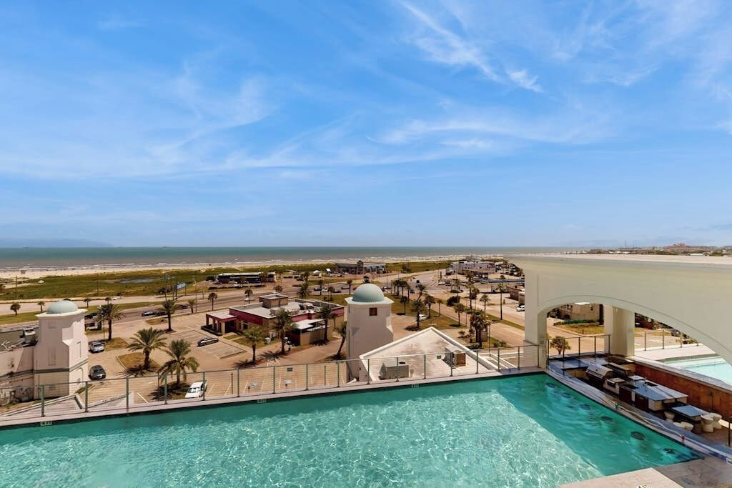 A pool area with a view of the beach and ocean, surrounded by buildings with domed structures.