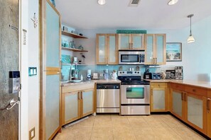 A modern kitchen with stainless steel appliances, wooden cabinets, and a tiled backsplash. - Emerald by the Sea #711 (Galveston)
