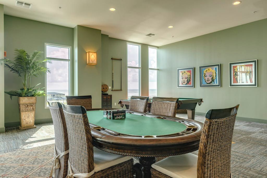 Une pièce avec une table de billard, des fauteuils en osier et des œuvres d’art encadrées accrochées au mur.
