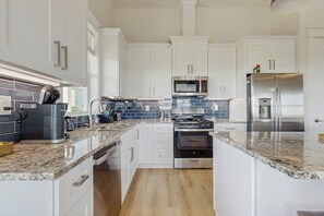 A modern kitchen with white cabinets, a stainless steel refrigerator, a microwave, and a stove. - Wishing Star - Hot Tub, Gulf Views, Steps to Sand (Galveston)