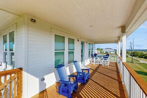 Een overdekt terras met houten vloer, witte muren en blauwe Adirondack-stoelen.