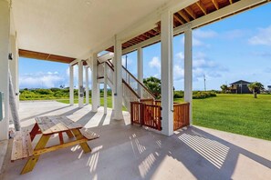 A covered outdoor area with a picnic table, a staircase, and a view of a green landscape. - Wishing Star - Hot Tub, Gulf Views, Steps to Sand (Galveston)