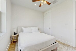 A bedroom with a bed, a nightstand, a ceiling fan, and a door. - Wishing Star - Hot Tub, Gulf Views, Steps to Sand (Galveston)