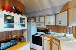 Una cocina compacta con armarios blancos, microondas, estufa, tostadora y pileta.