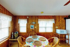 A dining area with a round table, four chairs, a microwave, and a fish decoration on the wall. - Long Island Village 214 Bonnet (Port Isabel)