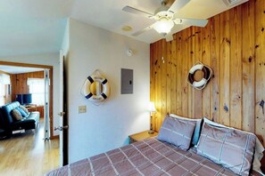 A bedroom with a bed, wooden wall paneling, a ceiling fan, and two life rings on the wall. - Long Island Village 214 Bonnet (Port Isabel)