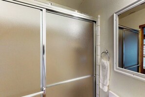A bathroom with a frosted glass shower door, a towel hanging on a rack, and a window with a view. - Long Island Village 214 Bonnet (Port Isabel)