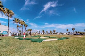 Campo de golfe com putting green, palmeiras e céu claro.