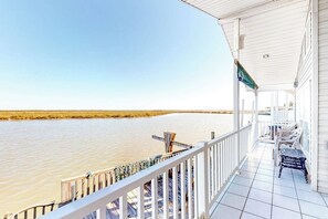A covered porch with a view of a calm body of water, a railing, and a bench. - Long Island Village 638 Sand Dollar (Port Isabel)
