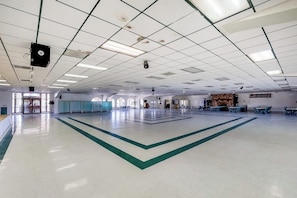 Àmplia zona interior amb sostre alt, llums múltiples fixades al sostre i un espai central obert amb un disseny geomàtric verd al sòl.