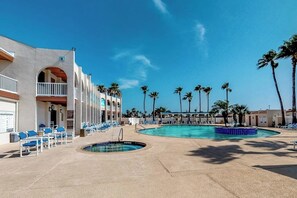 A hotel pool area with multiple lounge chairs, a small pool, and palm trees. - Long Island Village 638 Sand Dollar (Port Isabel)