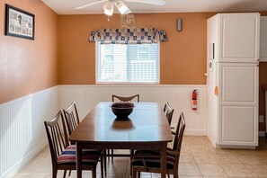 A dining area with a wooden table and chairs, a window with blinds, a white refrigerator, and a ceiling fan. - Long Island Village 638 Sand Dollar (Port Isabel)