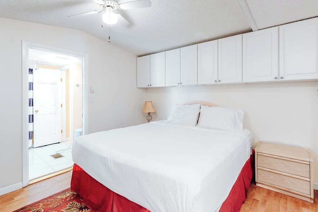 A bedroom with a bed, a nightstand, a ceiling fan, and a door leading to a bathroom.