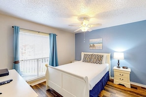 A bedroom with a bed, a nightstand, a ceiling fan, a window with curtains, and a painting on the wall. - Beach Club 363 - Heated Pool & Hot Tub, Dogs OK (Corpus Christi)
