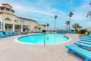 A pool area with blue lounge chairs and a building with a balcony. - Beach Club - Resting Beach Face (Corpus Christi)