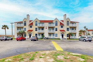 A multi-story hotel with a symmetrical facade, balconies, and a parking lot with several cars. - Beach Club - Resting Beach Face (Corpus Christi)
