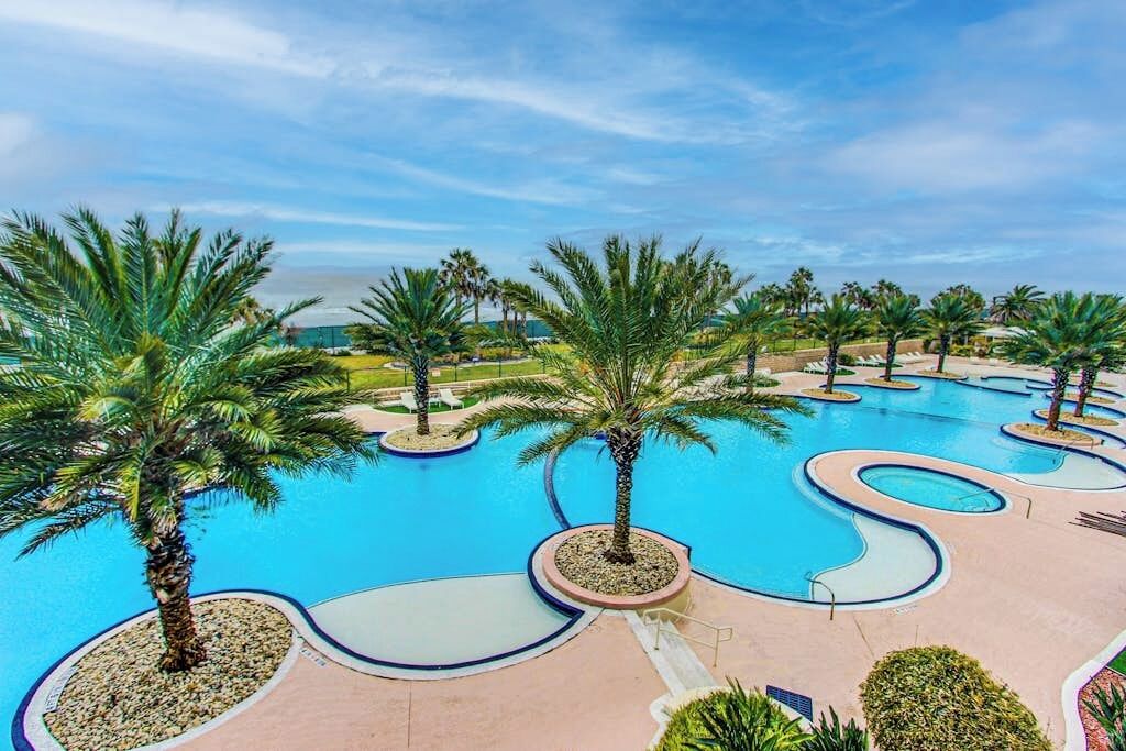 A resort pool area with palm trees and a clear sky.
