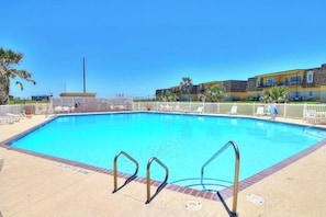 A clear blue pool with metal ladders, surrounded by a white fence and palm trees. - Unit 32, Island Retreat Resort (Port Aransas)