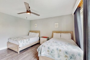 Ein Zimmer mit zwei Einzelbetten, einem Deckenventilator und einem Nachttisch mit einem roten Gegenstand.